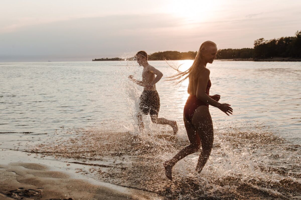 Two teenagers running on a beach at sunset, enjoying the summer seaside with splashes.