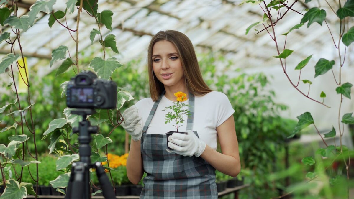 Young gardener filming a plant care tutorial in a bright greenhouse setting.